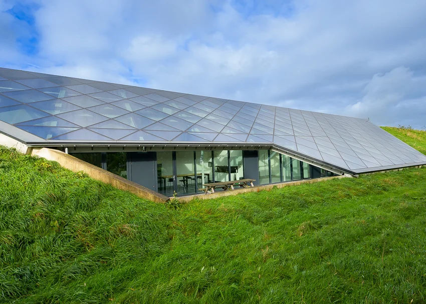 Modern gebouw met een hellend glazen dak, deels ingebouwd in een grasheuvel, bij het Mart Stamhof.